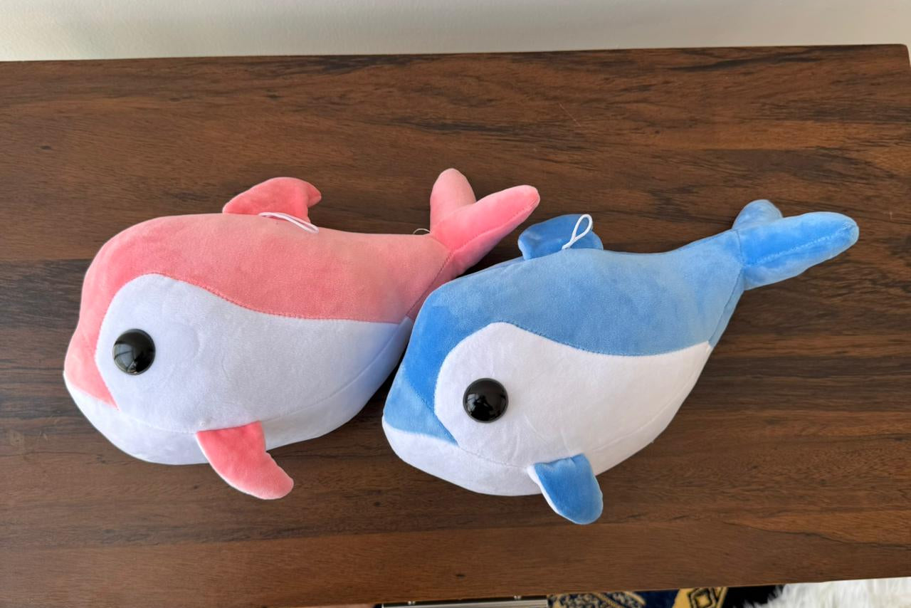 Two plush dolphins, one pink and one blue, on a wooden surface.