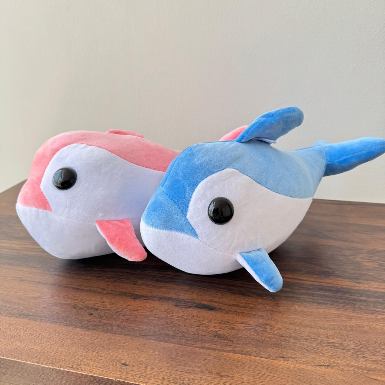 Two plush toys resembling dolphins on a wooden surface with a neutral background