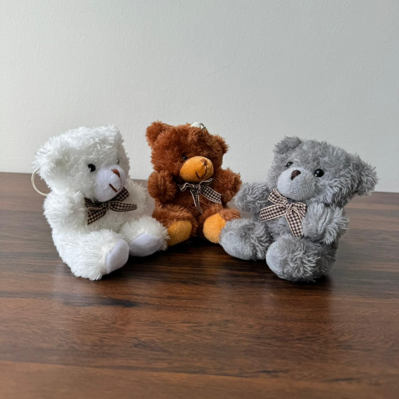 Three teddy bears in white, brown, and gray sitting on a wooden surface with a plain background.