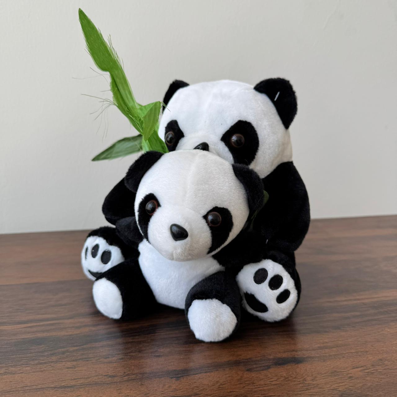 Two panda plush toys sitting together on a wooden surface with a bamboo leaf.