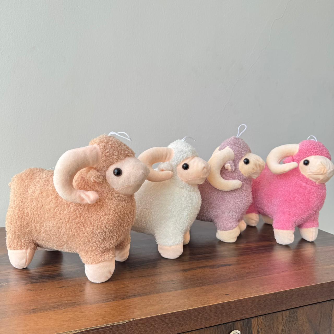 Four plush toy sheep in different colors lined up on a wooden surface with a gray background