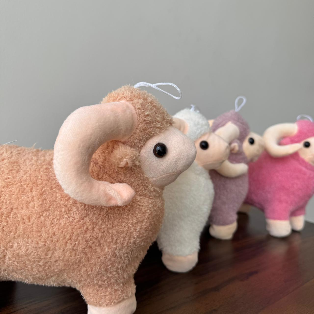 Four plush toy rams in different colors on a wooden surface with a gray background