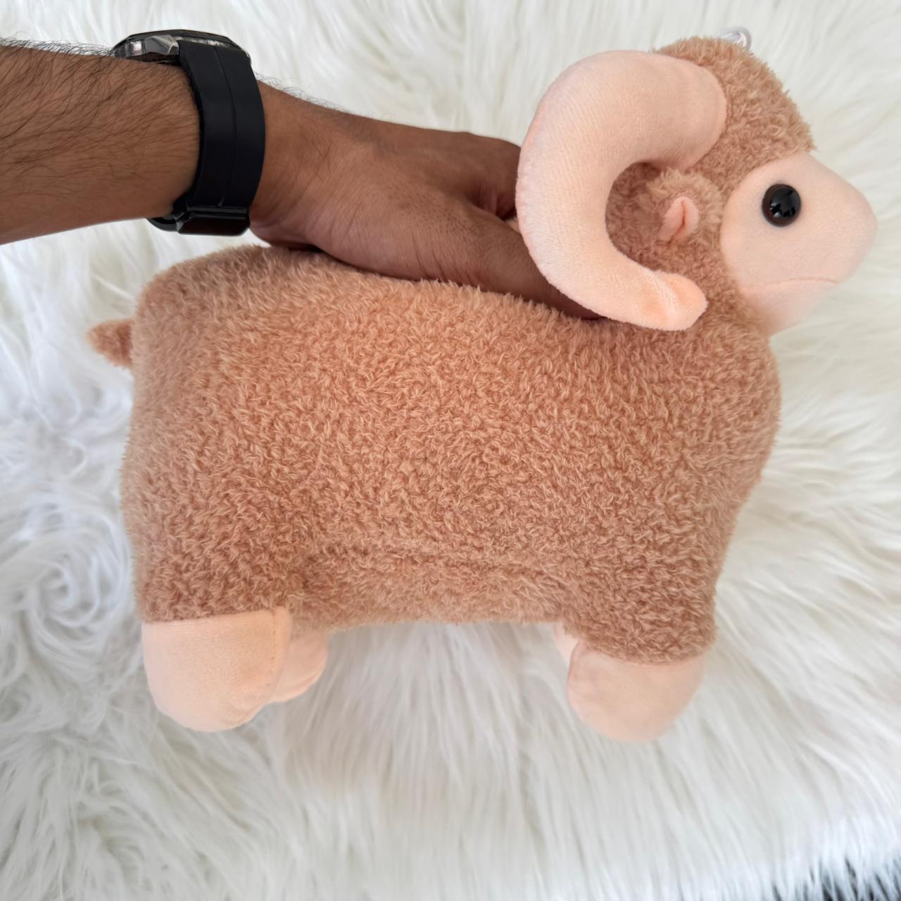 Plush toy ram held by a person on a white fluffy surface