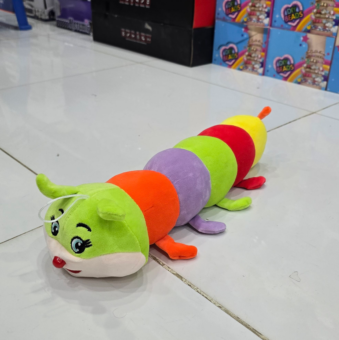 Colorful caterpillar-shaped plush toy on a tiled floor with boxes in the background