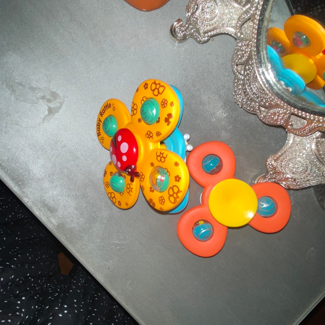 A colorful plastic toy with two butterfly-like pieces on a gray tabletop, alongside a silver decorative mirror and part of an orange object.